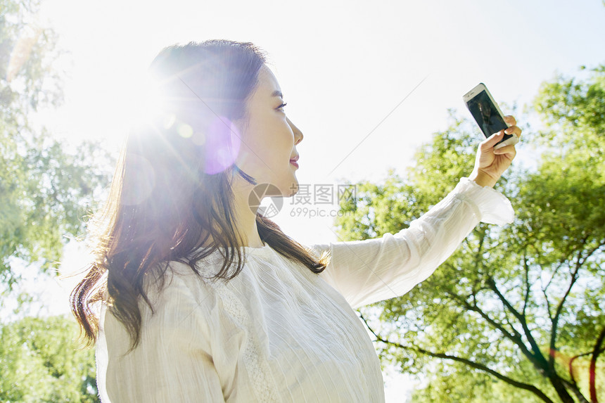 公园里拿着手机自拍的女性图片