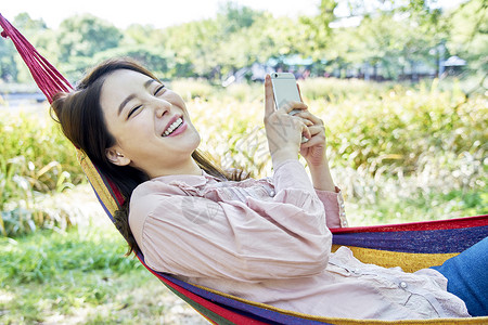 公园吊床上玩手机的年轻女子图片