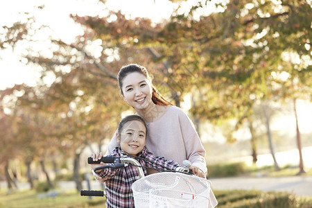 枫树下女孩母女骑行双人自行车游览公园背景