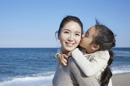 海边沙滩上在妈妈背上的女孩亲吻妈妈图片
