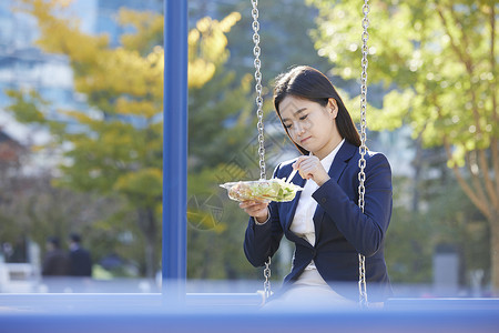 坐在公园吊椅上吃沙拉的女青年图片