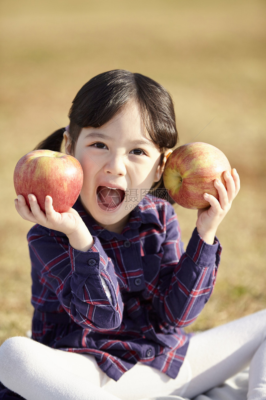 小女孩在户外草地上拿着苹果图片