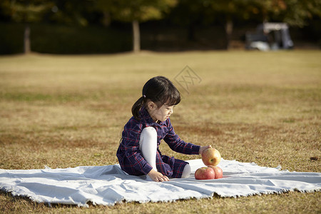 坐在野餐垫上的小女孩抱着苹果背景图片