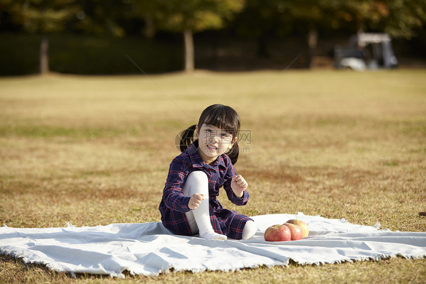 坐在野餐垫上的小女孩抱着苹果图片