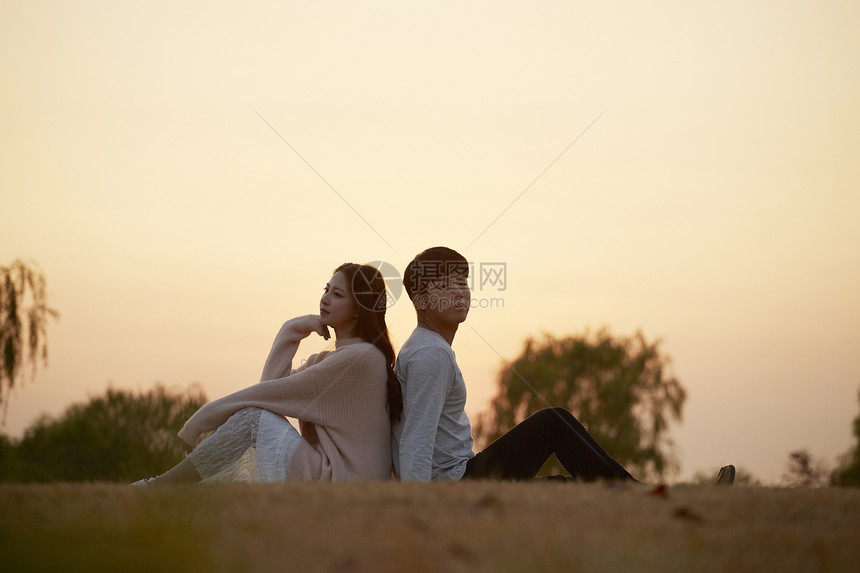 落日黄昏背靠背坐在草坪上的情侣图片
