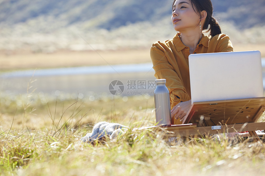 带着便携电脑旅行在草地上工作的女人图片