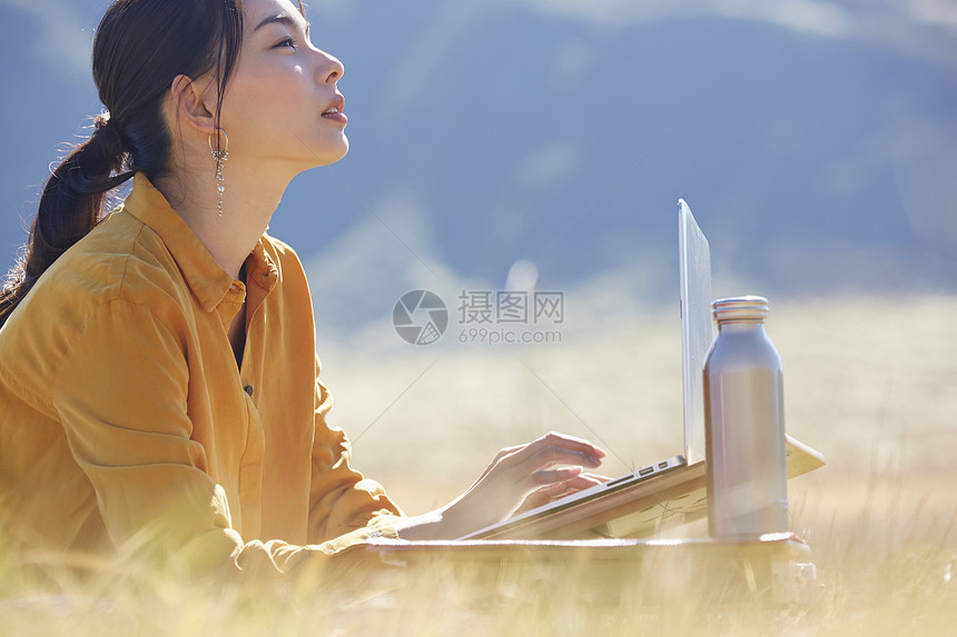 带着便携电脑旅行在草地上工作的女人图片