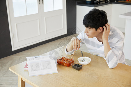 餐桌上吃饭看书的青年男子图片