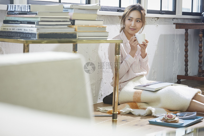 坐在地上喝茶看书的居家女性图片