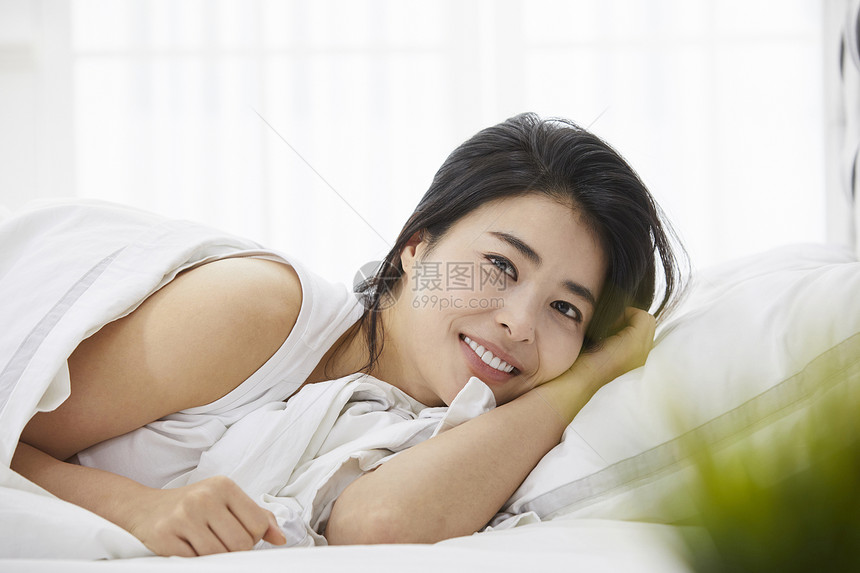 微笑的年轻女子躺在床上休息图片