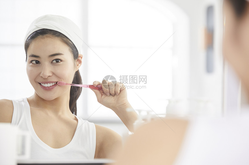 镜子前拿着牙膏洗漱的女青年图片