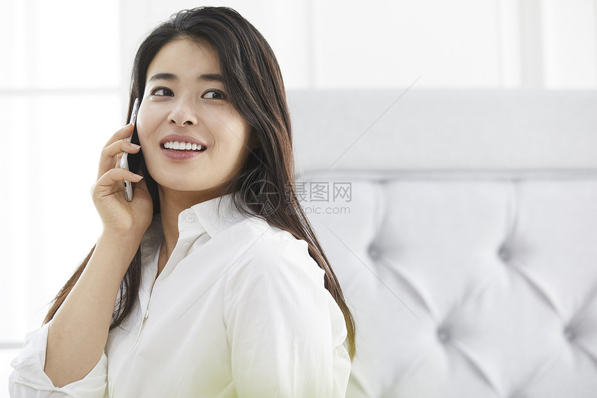 卧室里接电话微笑的年轻女子图片