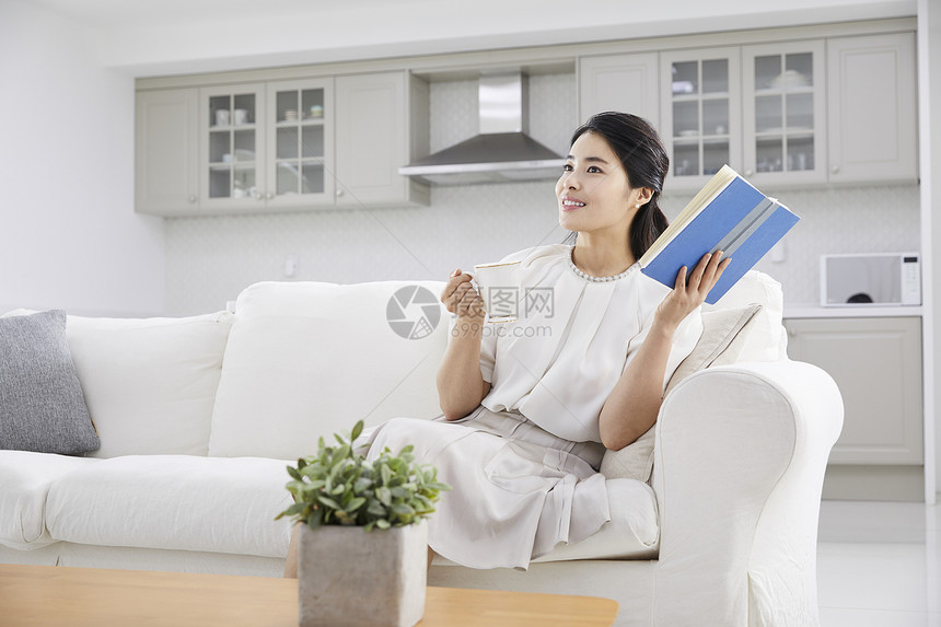 坐在沙发上喝茶阅读的女青年图片