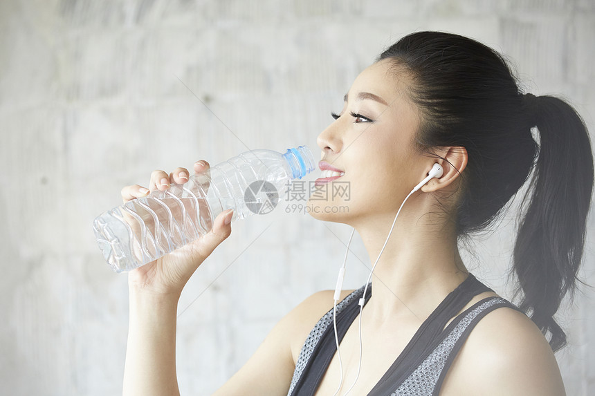 戴着耳机喝水休息的女青年图片