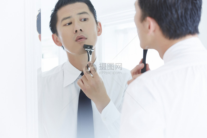 镜子前拿着剃须刀刮胡子的成年男子图片