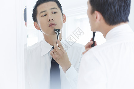 镜子前拿着剃须刀刮胡子的成年男子图片