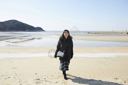 冬天穿着羽绒服海滩上散步的年轻女子图片