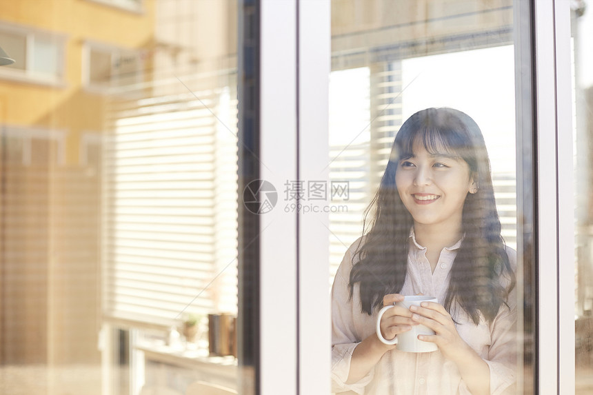 拿着咖啡看向窗外的年轻女子图片