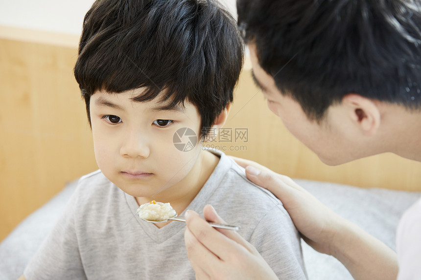 父亲拿着勺子喂食小男孩图片