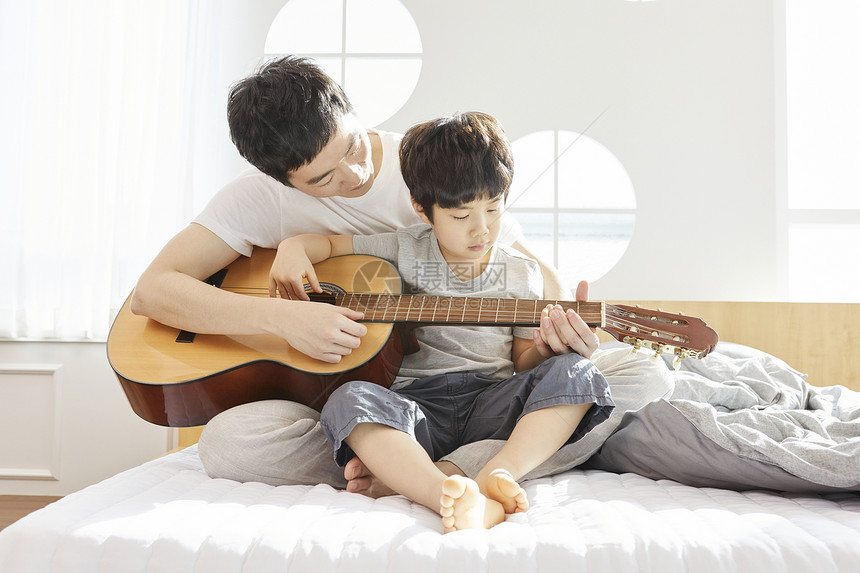 坐在床上一起弹吉他的父子图片