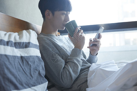坐在床上喝水看手机的青年男性图片