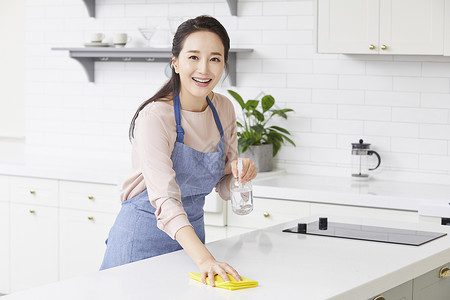 年轻女子拿着抹布和喷壶清洁桌面图片