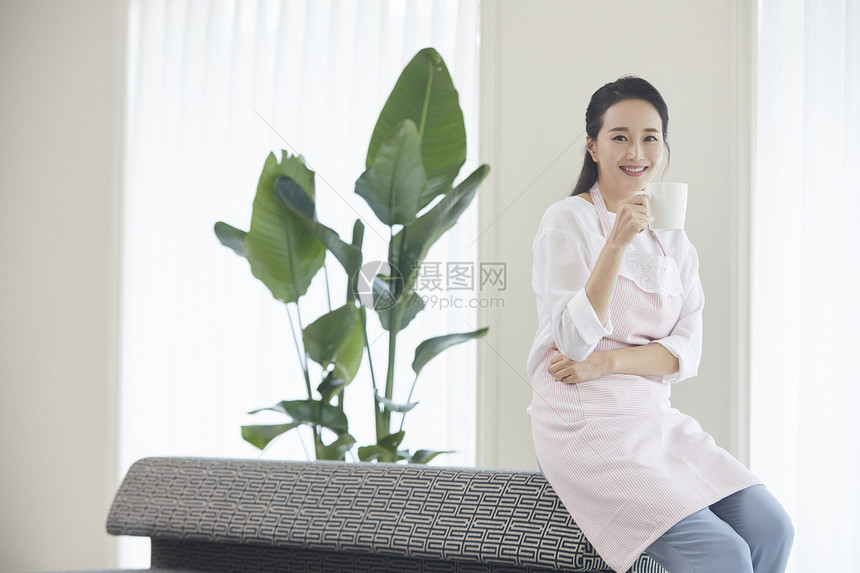 穿着围裙坐在沙发上喝咖啡休息的女青年图片