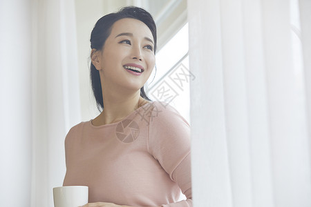 靠在窗边拿着咖啡微笑的成年女子图片