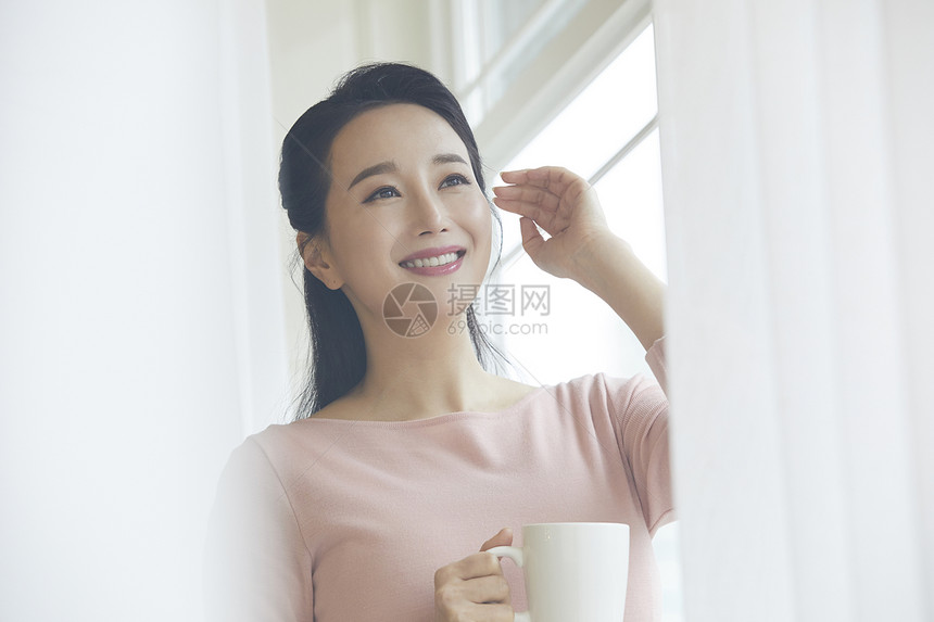 窗边拿着咖啡放松的成年女子图片