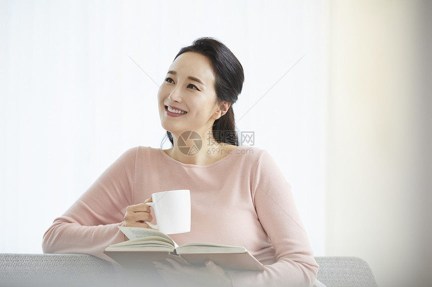 沙发上拿着书和咖啡的女青年图片