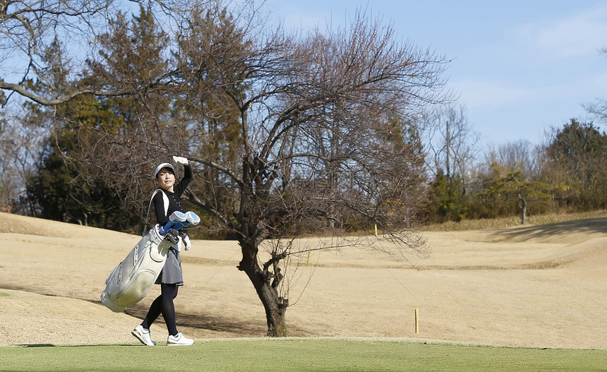 女子背着高尔夫球袋走在球场图片