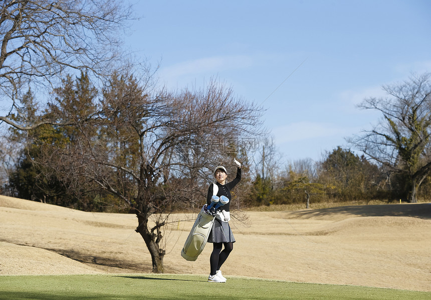 女子背着高尔夫球袋走在球场图片