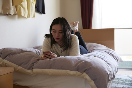 年轻女子趴在床上玩手机图片