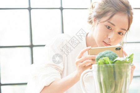 手机拍蔬菜榨汁机的年轻女子图片