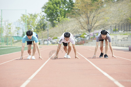 三个青年在跑道上准备起跑高清图片