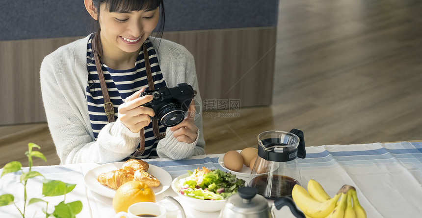 餐桌上拿着相机的年轻女子图片