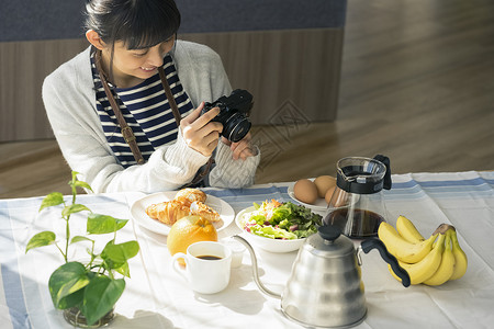 餐桌上拿着相机拍照的年轻女子图片