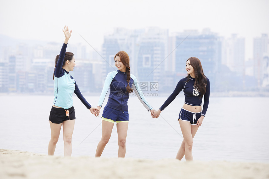 三个年轻女人在海边沙滩上手牵手散步玩耍图片