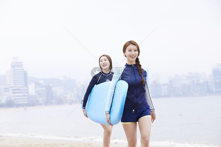 两个年轻女人在海边沙滩上抱着冲浪板图片