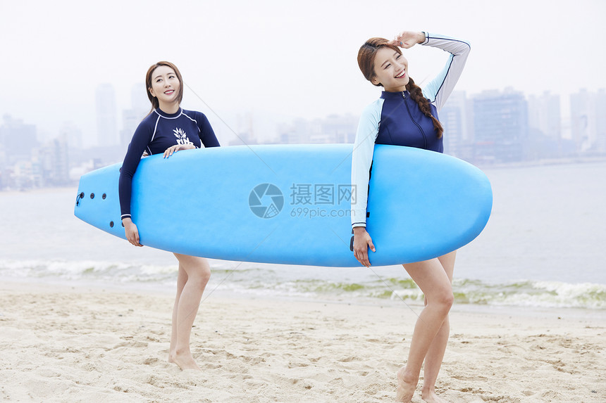 两个年轻女人在海边沙滩上抱着冲浪板图片