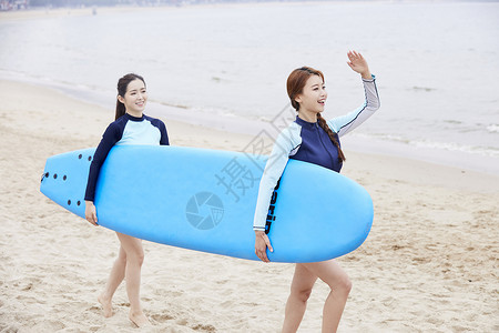 两个年轻女人在海边沙滩上抱着冲浪板图片