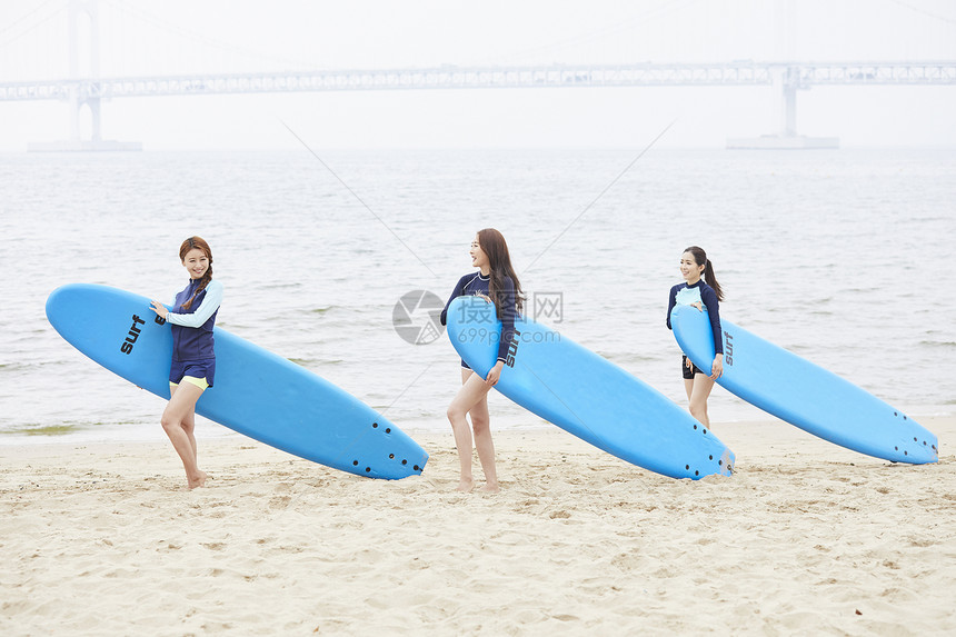 三个年轻女人在海边沙滩上抱着冲浪板图片
