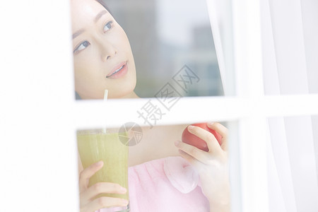 拿着蔬菜汁看向窗外的年轻女子图片