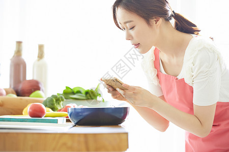 厨房里拿着手机拍食物的年轻女子图片