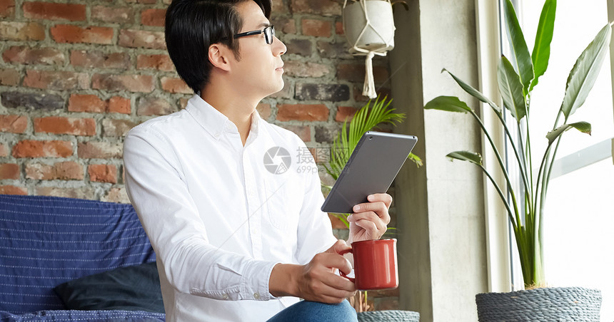 公寓里查看平板电脑喝茶的男人图片