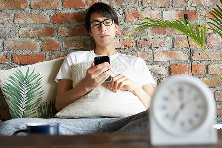 戴眼镜的男人坐在沙发上看手机图片