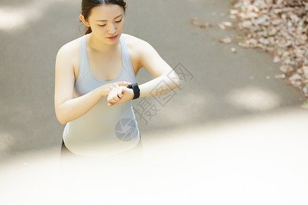 公园里跑步低头看着手表的女青年图片