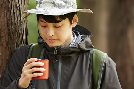 男青年靠在树上低头看着水杯图片