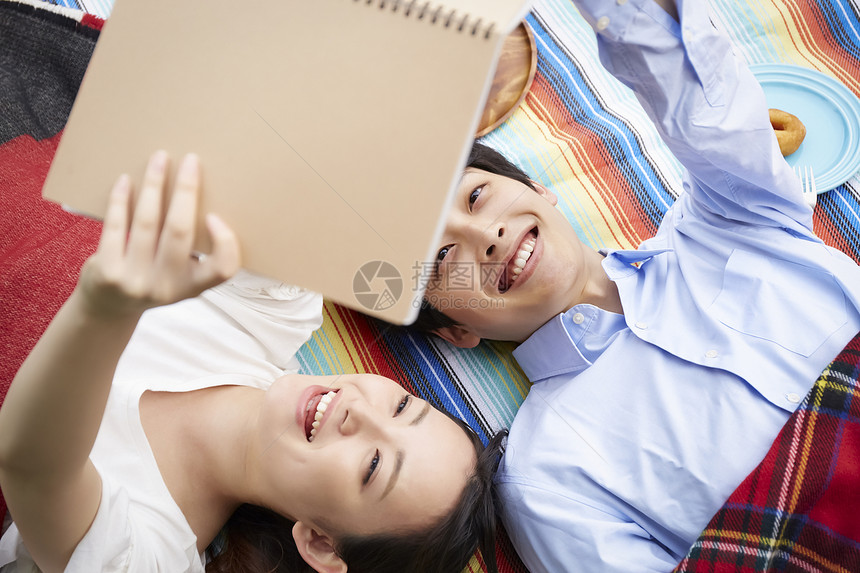 躺在野餐垫上看书休息的情侣图片