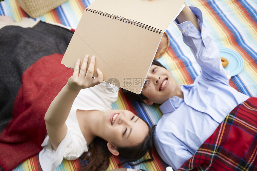 青年情侣躺在野餐垫上看书图片